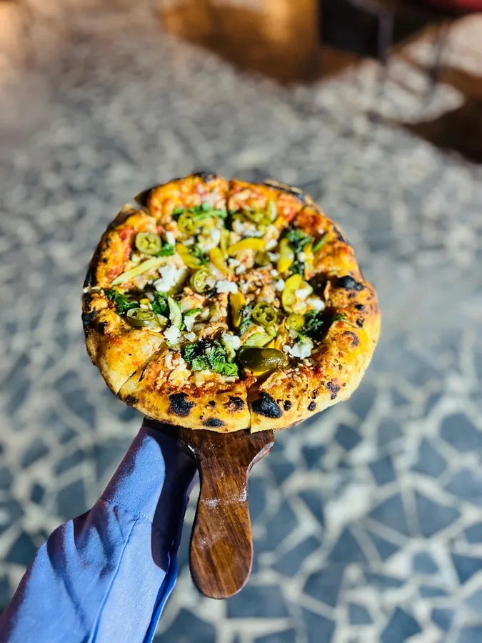 Wood-fired Mediterranean pizza with jalapeños, olives and arugula on a serving paddle